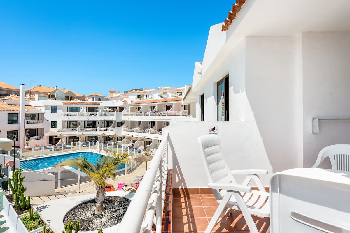 Un balcon d’hôtel avec une piscine, des chaises blanches et une vue sur d’autres immeubles.