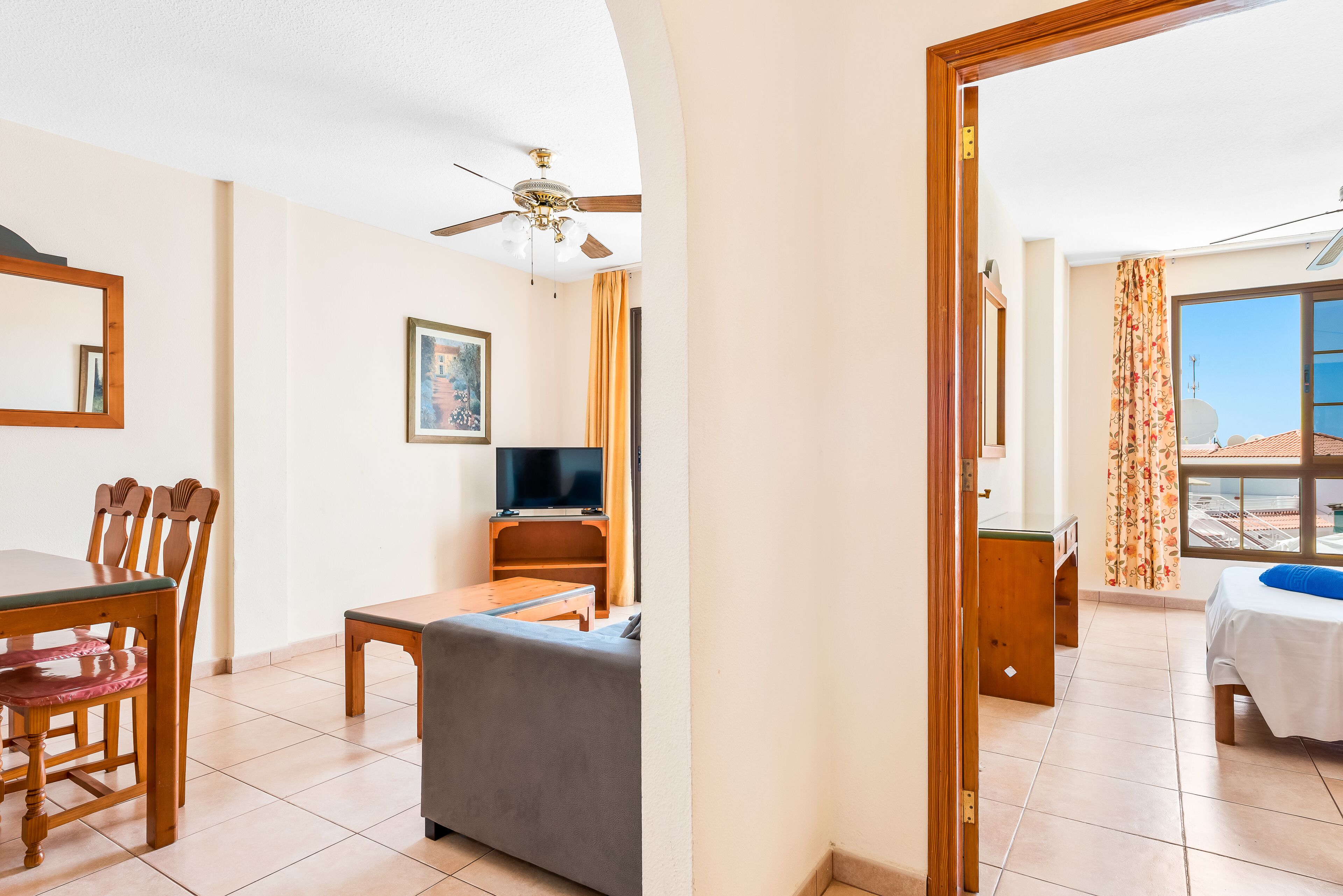A hotel room with a dining table, chairs, a sofa, a TV, and a balcony with a view.