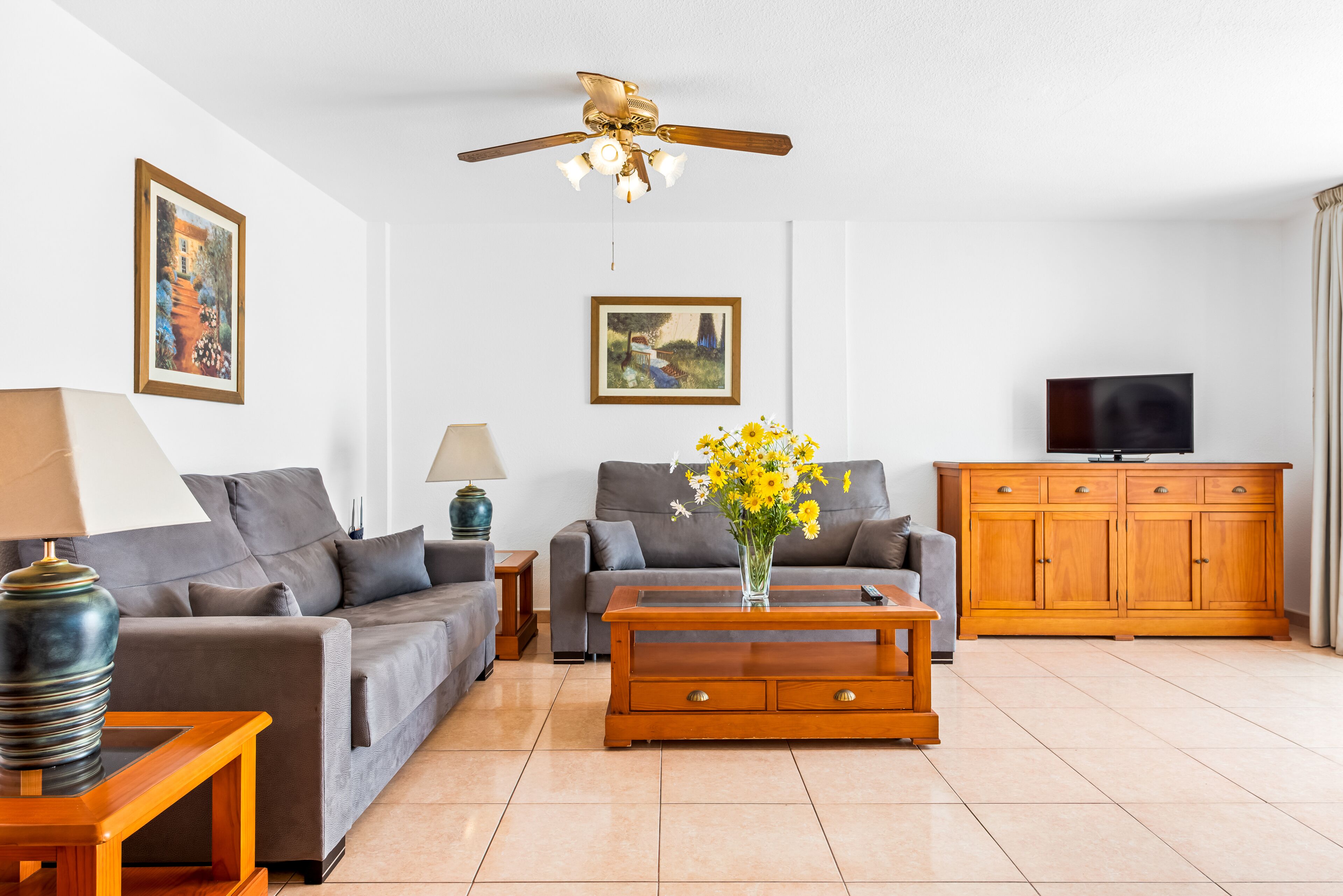 A living room with two sofas, a coffee table, a TV cabinet, and a ceiling fan.