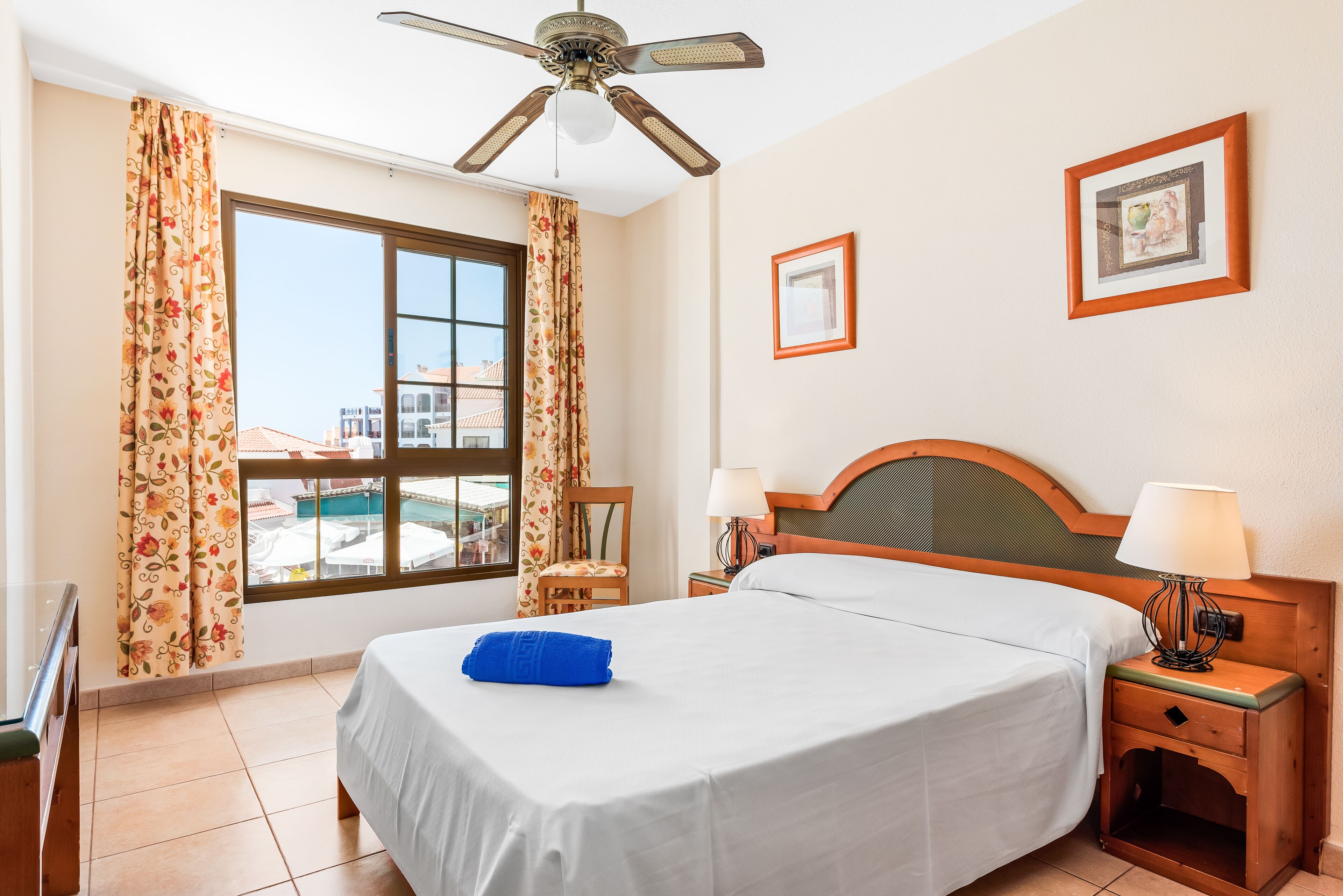 A hotel room with a bed, a nightstand, a lamp, a ceiling fan, and a window with curtains.
