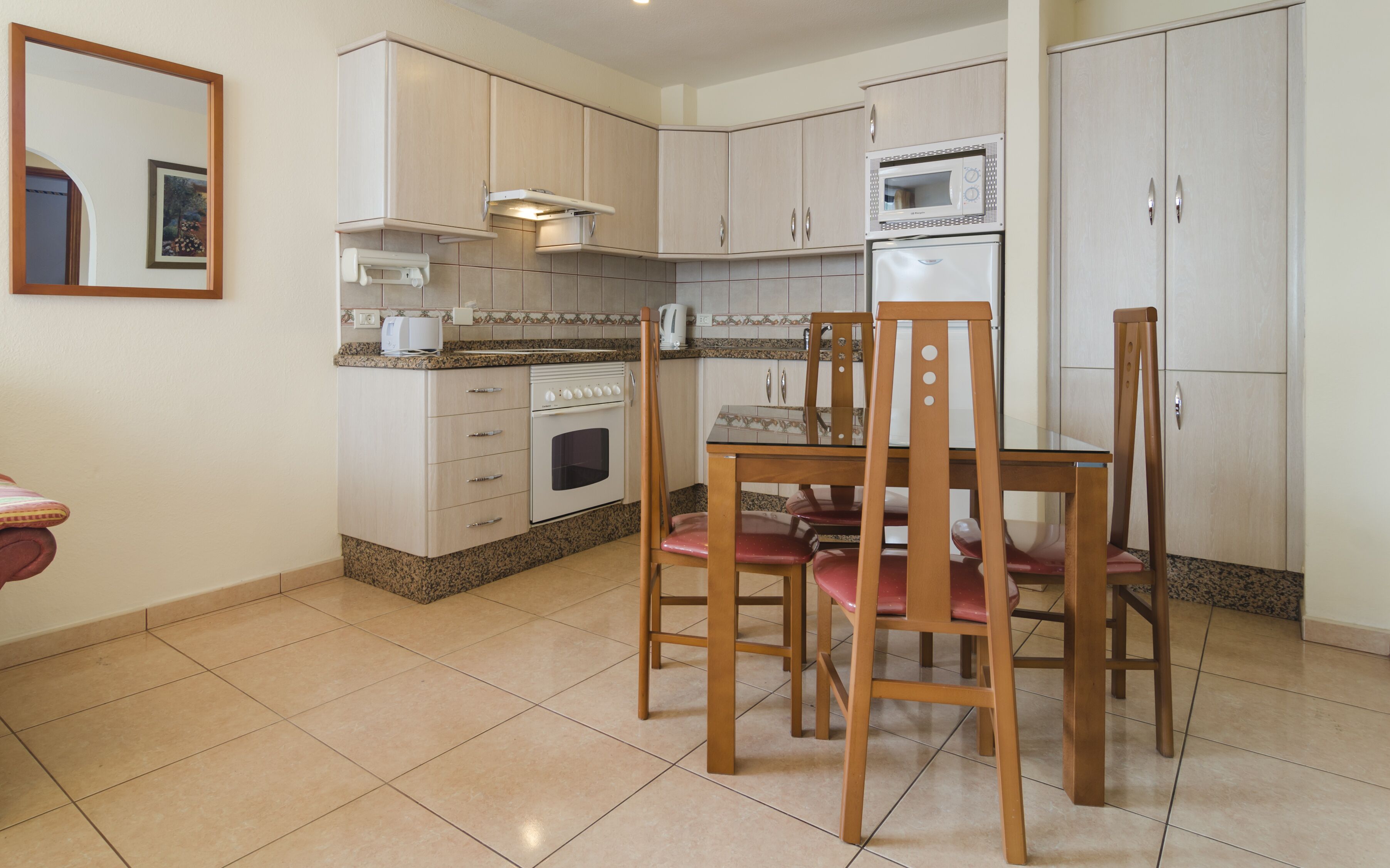 A compact kitchen with white cabinets, a microwave, and a stove. There is a dining table with chairs.