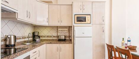 Cocina compacta equipada con microondas, estufa y refrigerador. Hay una mesa de comedor con sillas y una cafetera sobre la encimera.