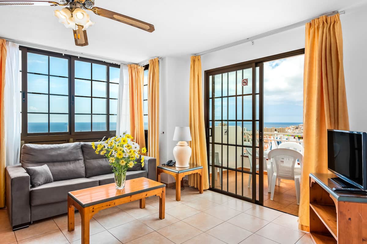 Un salon avec un canapé, une table basse, un téléviseur et un balcon offrant une vue agréable.