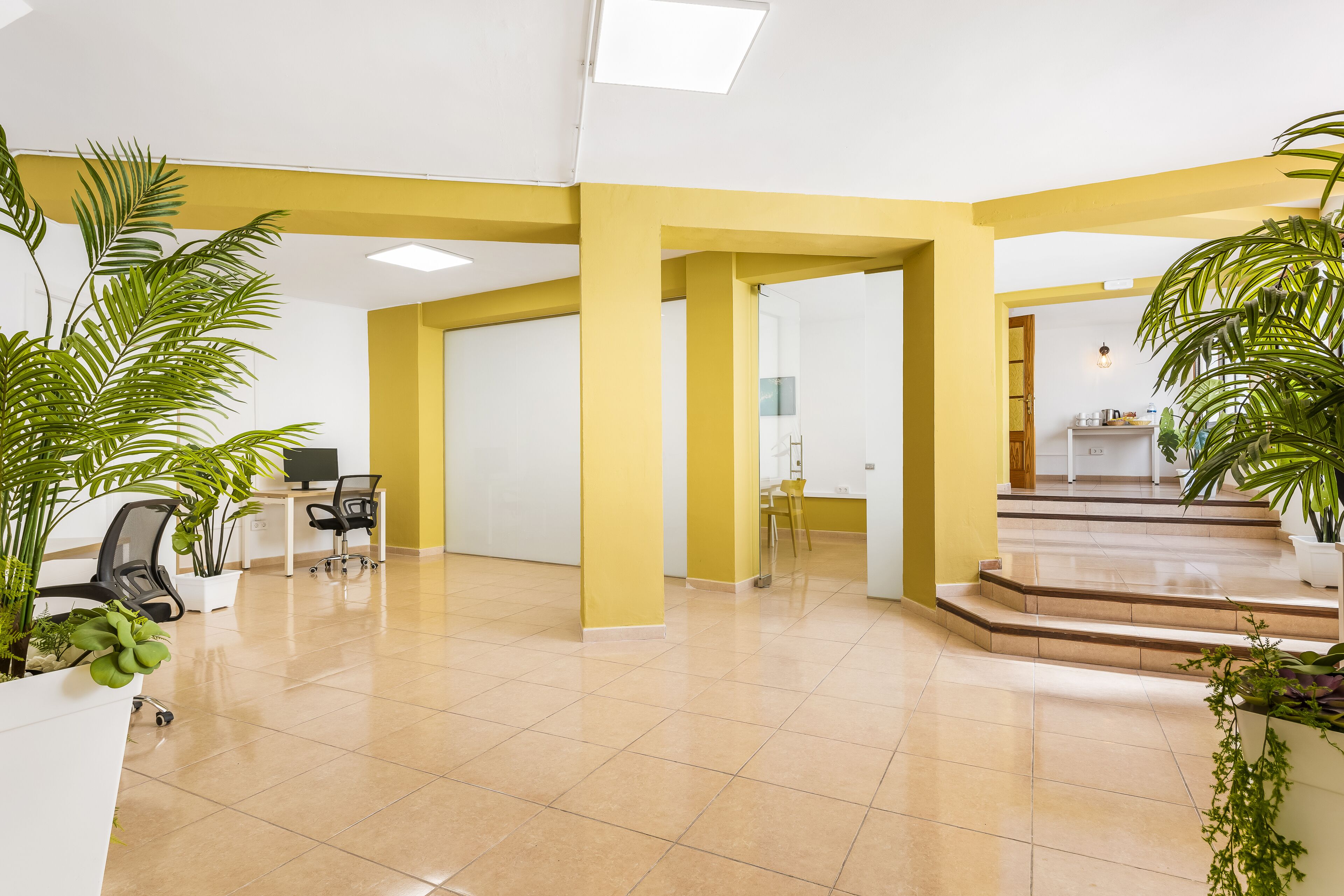 Een ruime lobby met gele zuilen, een receptiebalie en potplanten.