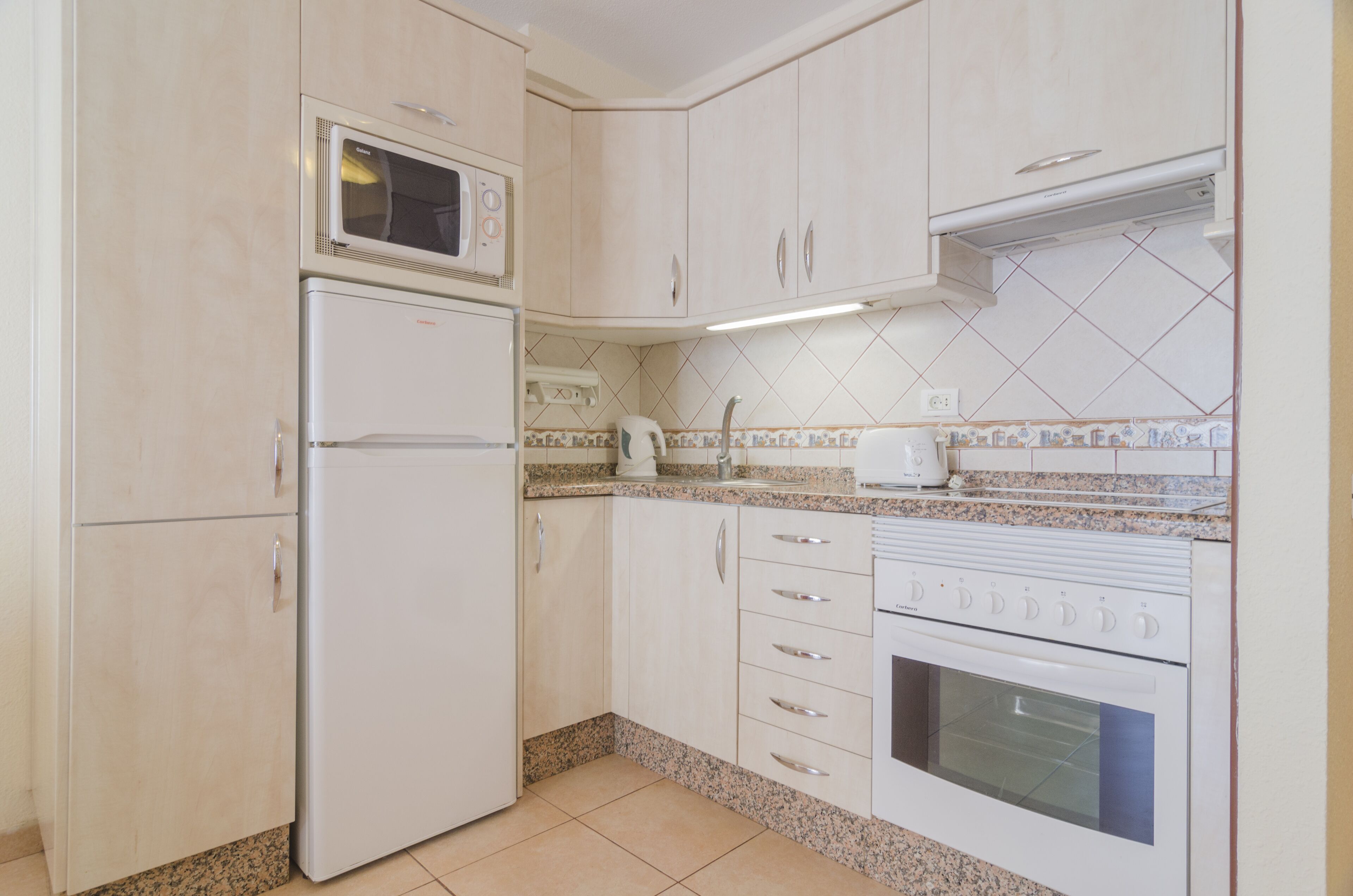 Una cocina con armarios blancos, microondas, refrigerador, estufa y salpicadero de azulejos.