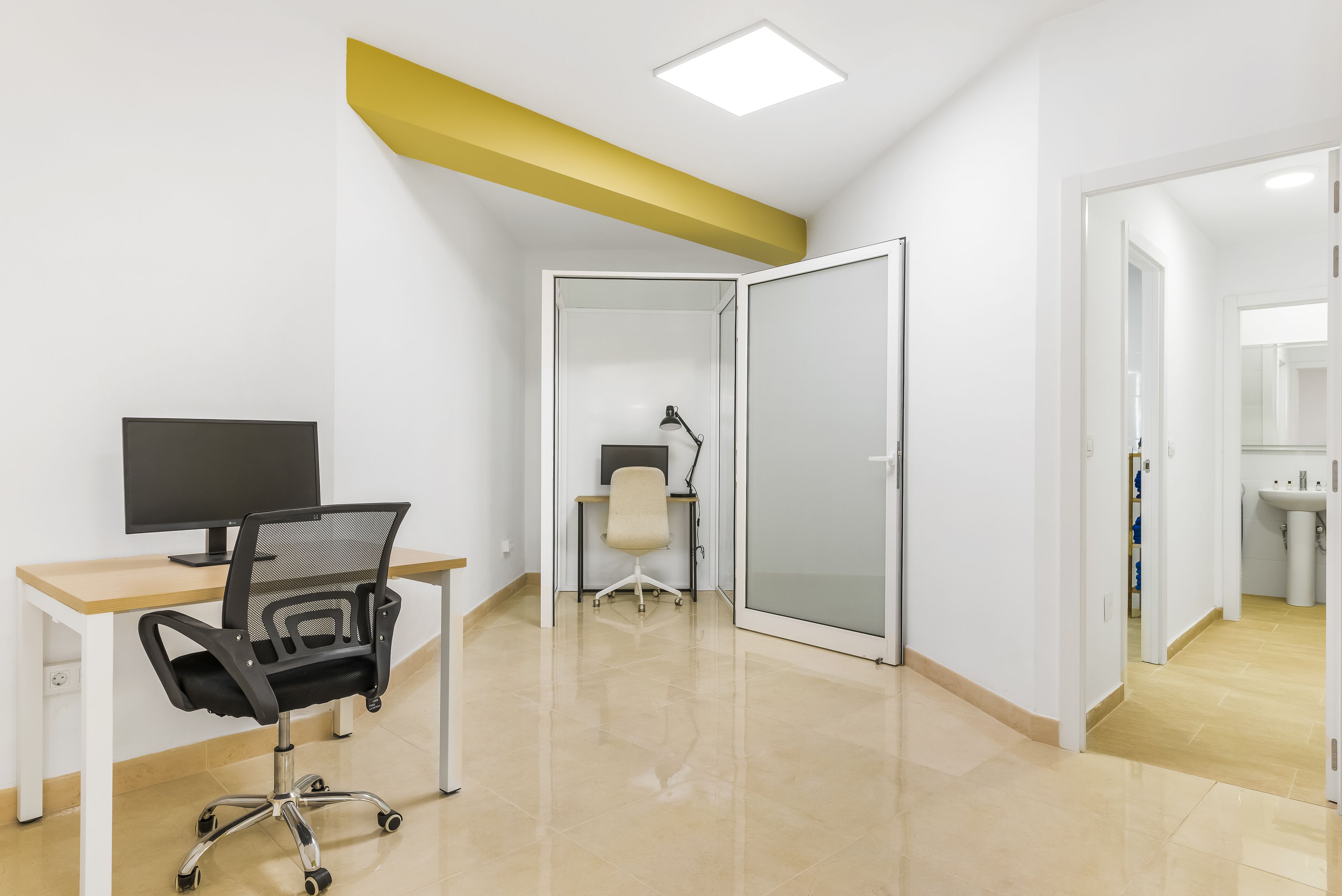 A modern office space with a desk, office chair, computer, and a glass partition wall.