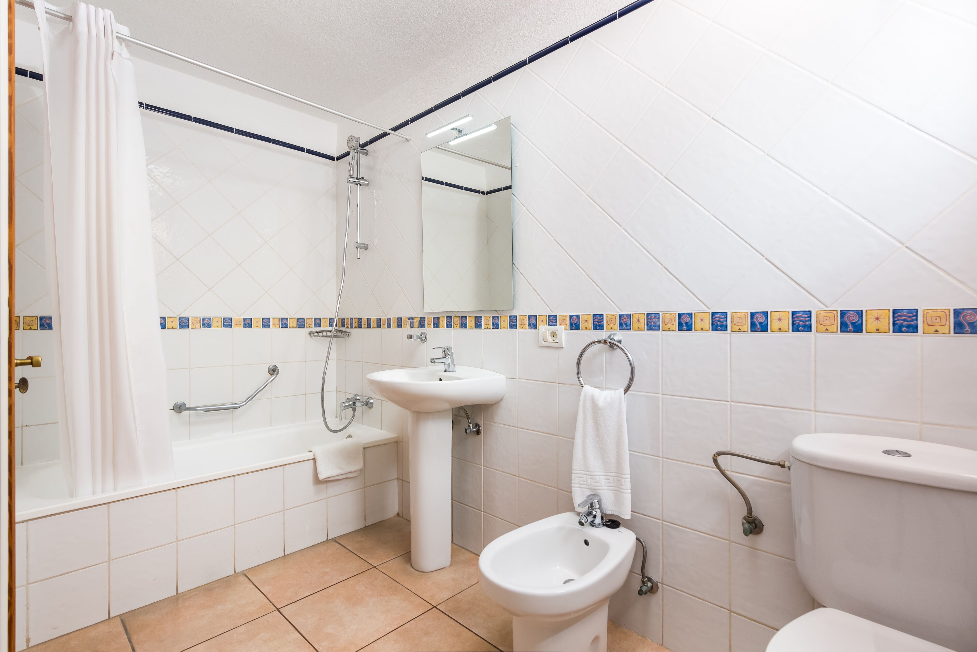 Een badkamer met een bad, wastafel, bidet, toilet en een spiegel.