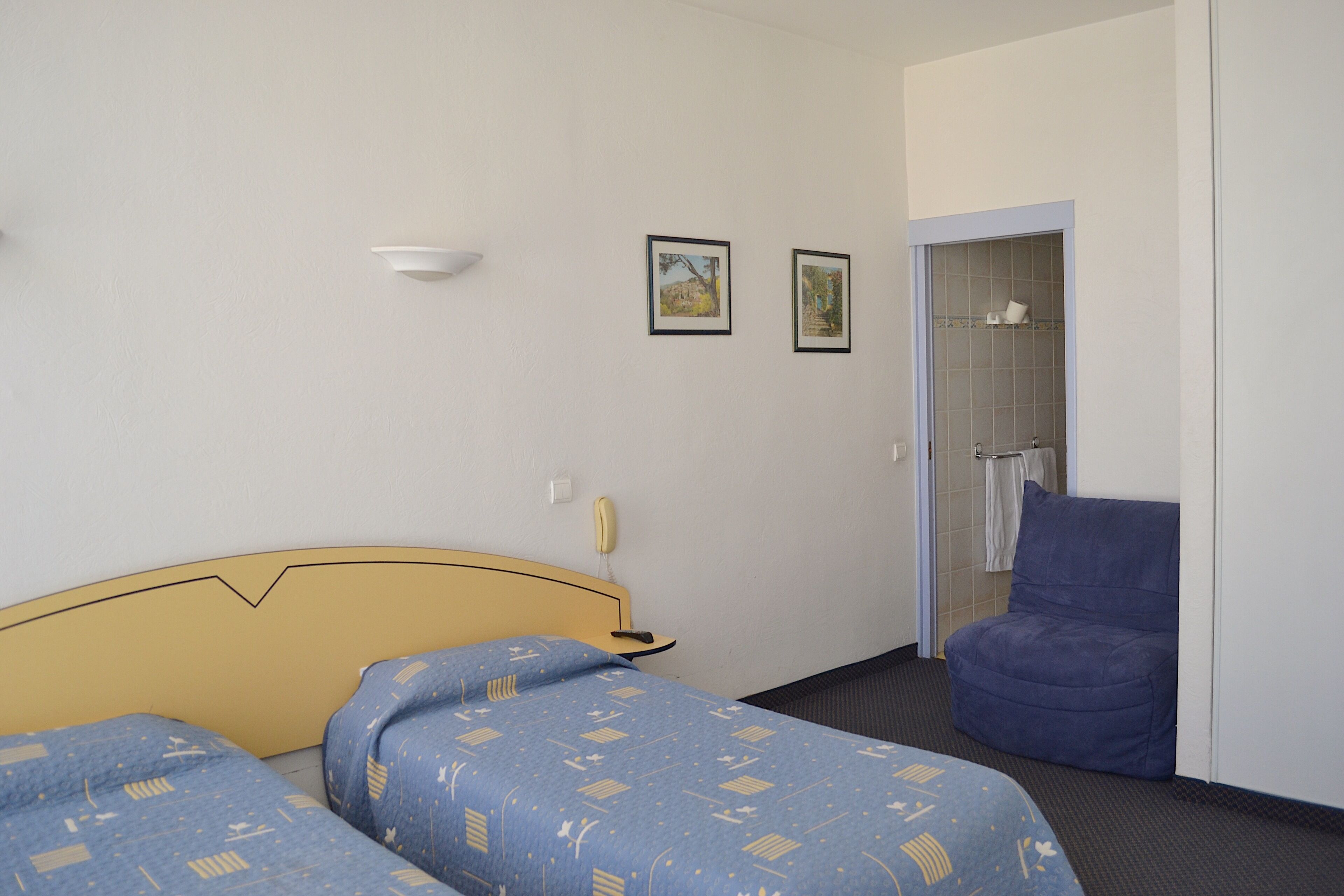 Une chambre d’hôtel avec deux lits, une chaise, un espace douche et une petite table avec un téléphone.