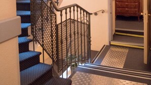 A staircase with a metal railing and a wooden door leading to a room with a dresser. - Modern Hôtel (Antibes)