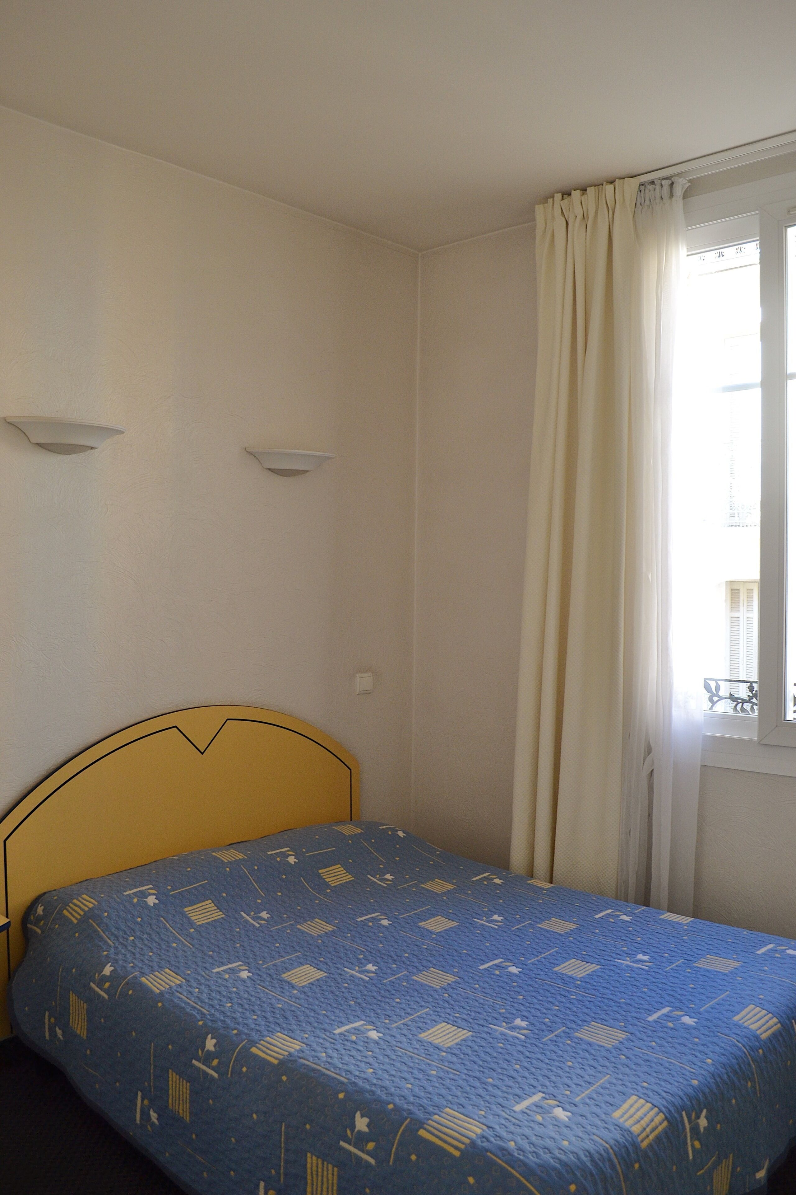 Una habitación con cama, ventana con cortinas e iluminación en la pared.