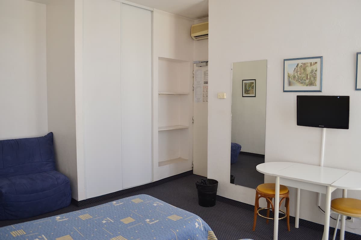 Habitación de hotel con cama, escritorio con dos taburetes, armario, espejo y televisor de pantalla plana.