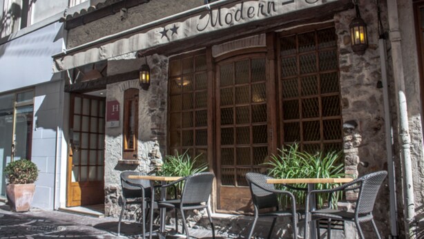A stone building with a sign reading "Modern Hotel." There are outdoor tables and chairs, and a potted plant is visible. - Modern Hôtel (Antibes)