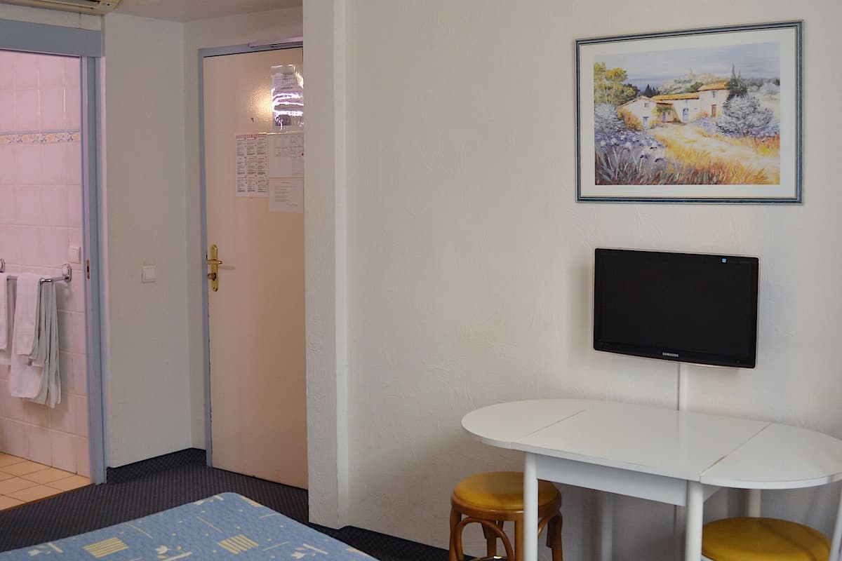 Una habitación de hotel con dos camas, un escritorio con una silla, una televisión y un cuadro en la pared.