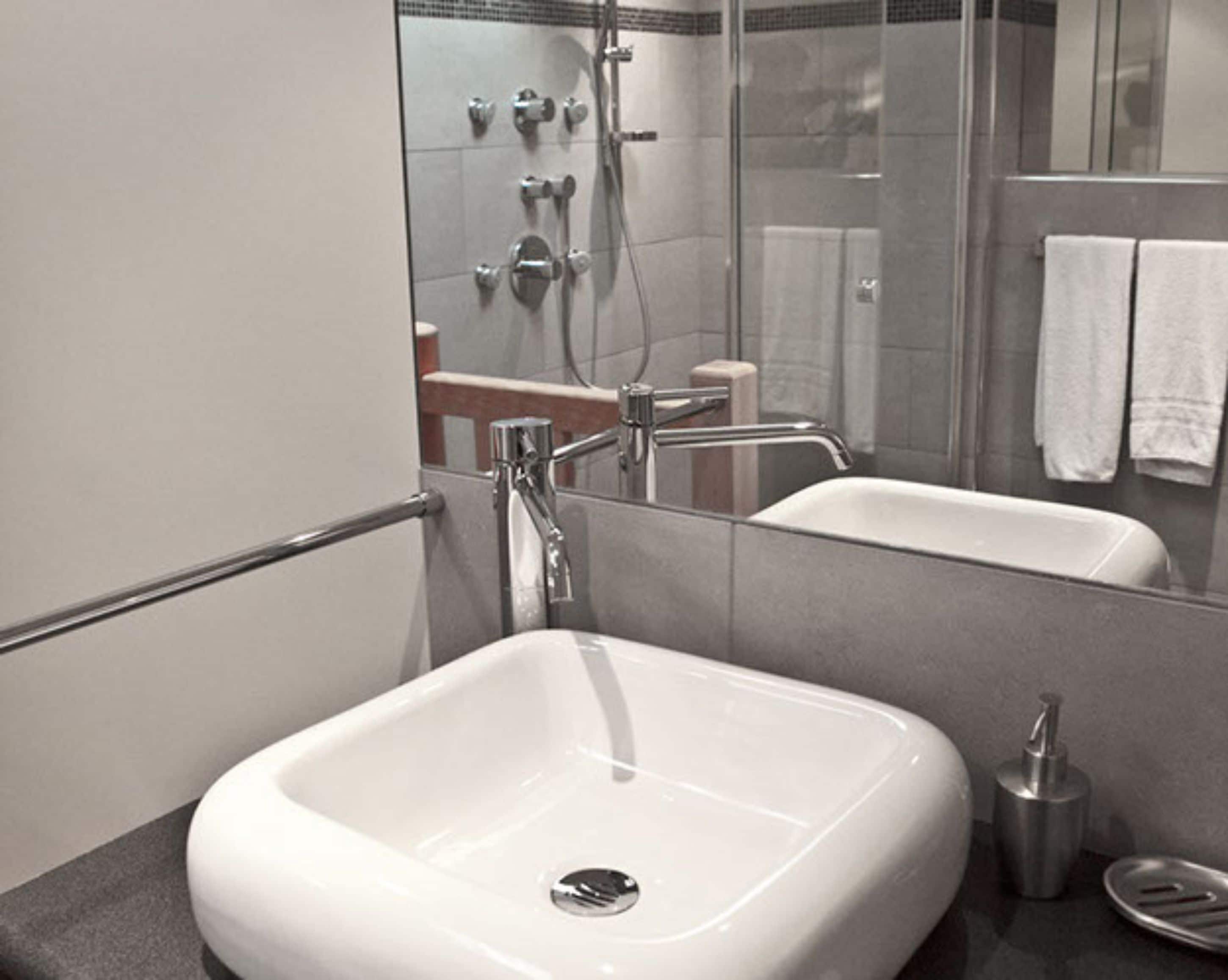 A modern bathroom with a white sink, a glass shower enclosure, and a mirror reflecting the space.