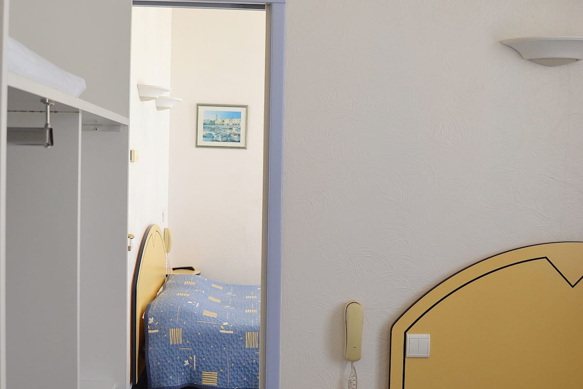 Una habitación de hotel con una cama, una mesita de noche con lámpara y un ventanal pequeño.