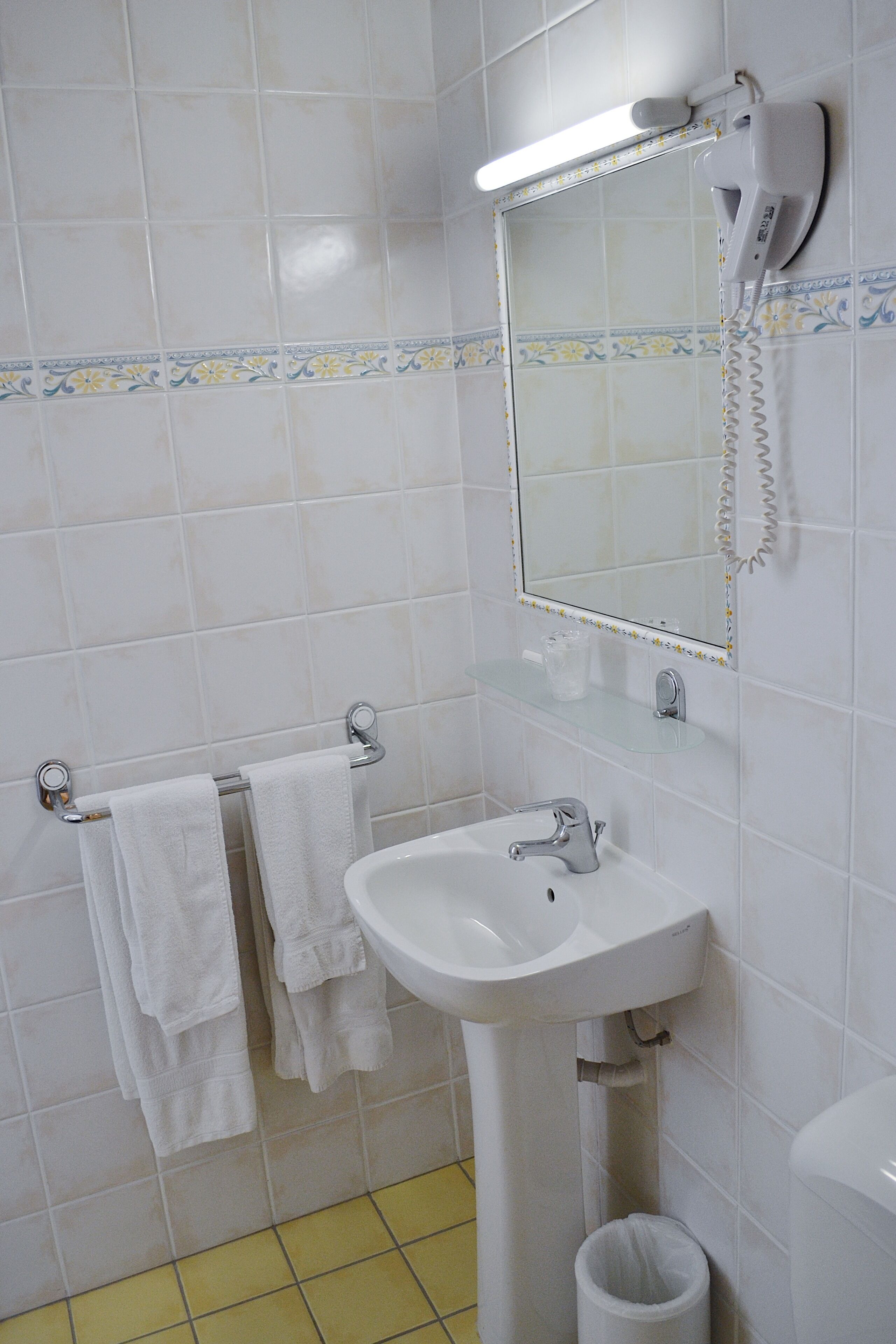 Une salle de bain avec un lavabo blanc, un miroir, un sèche-cheveux et un porte-serviettes.