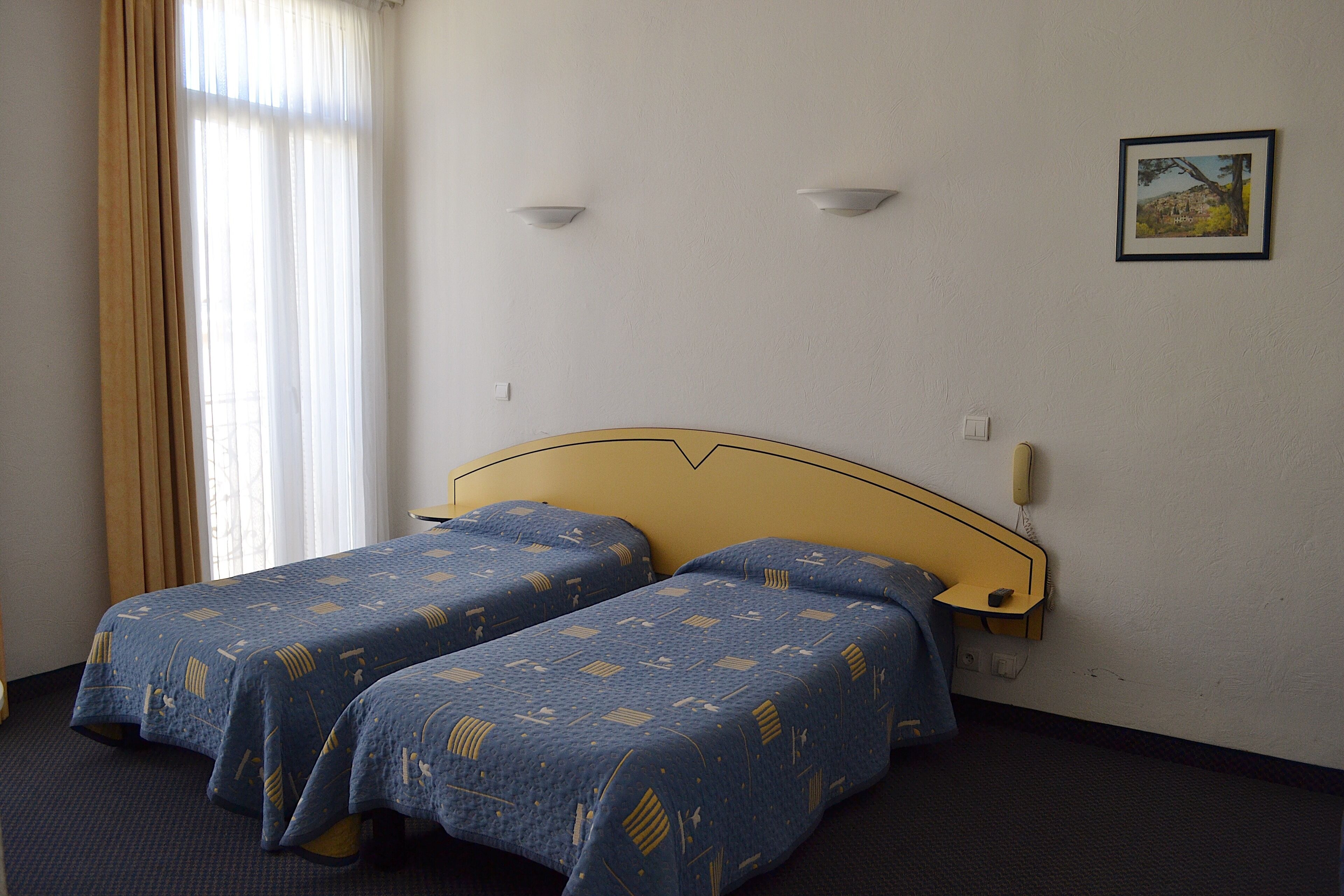 Ein Hotelzimmer mit zwei Betten, einem Kopfteil, einem Nachttisch, einem Telefon und einem Bild an der Wand.