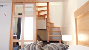 A bedroom with a bed, striped pillows, a wooden wardrobe, a mirror, and a staircase leading to an upper level. - Modern Hôtel (Antibes)