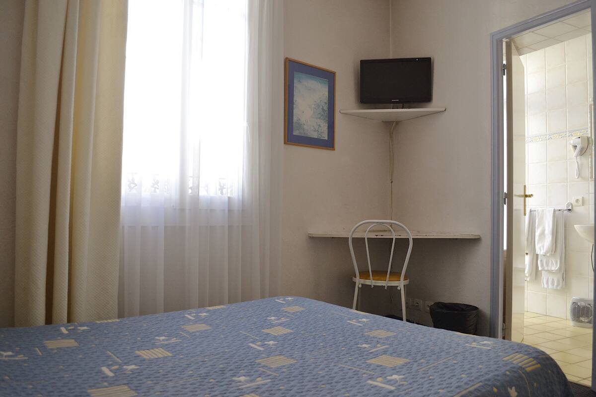 Habitación de hotel con una cama, una silla, un televisor y un baño visible a través de una puerta abierta.