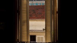 An open window with shutters, revealing a view of a building with a red-tiled roof and a chimney. - Modern Hôtel (Antibes)
