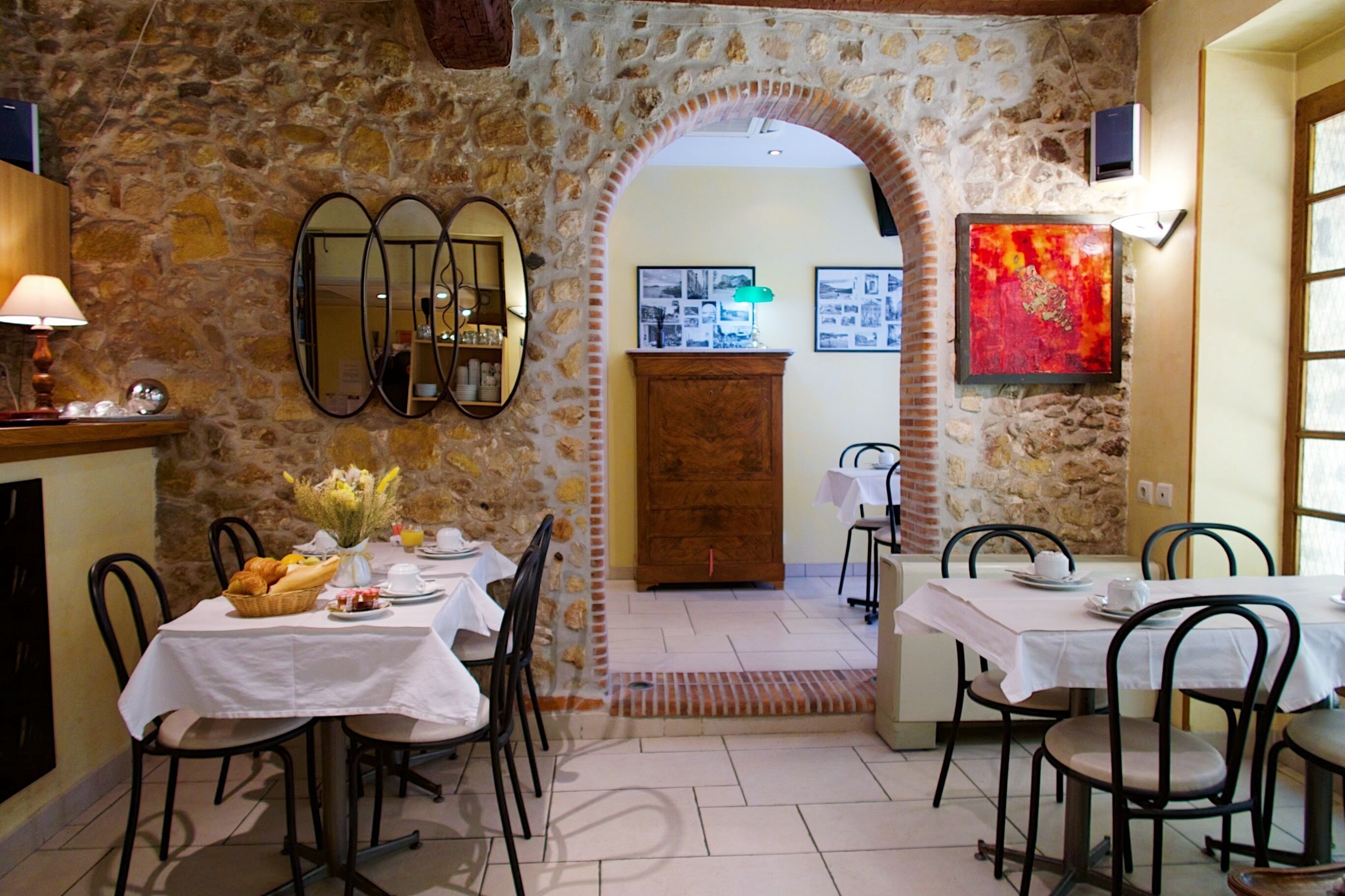 A dining area with stone walls, multiple tables, and chairs. There is a wooden cabinet and a mirror on the wall.