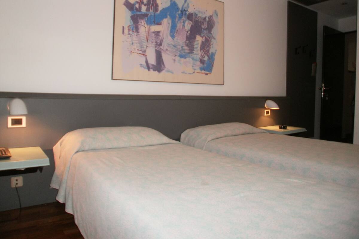 Una habitación de hotel con dos camas, un cuadro en la pared y lámparas de noche.