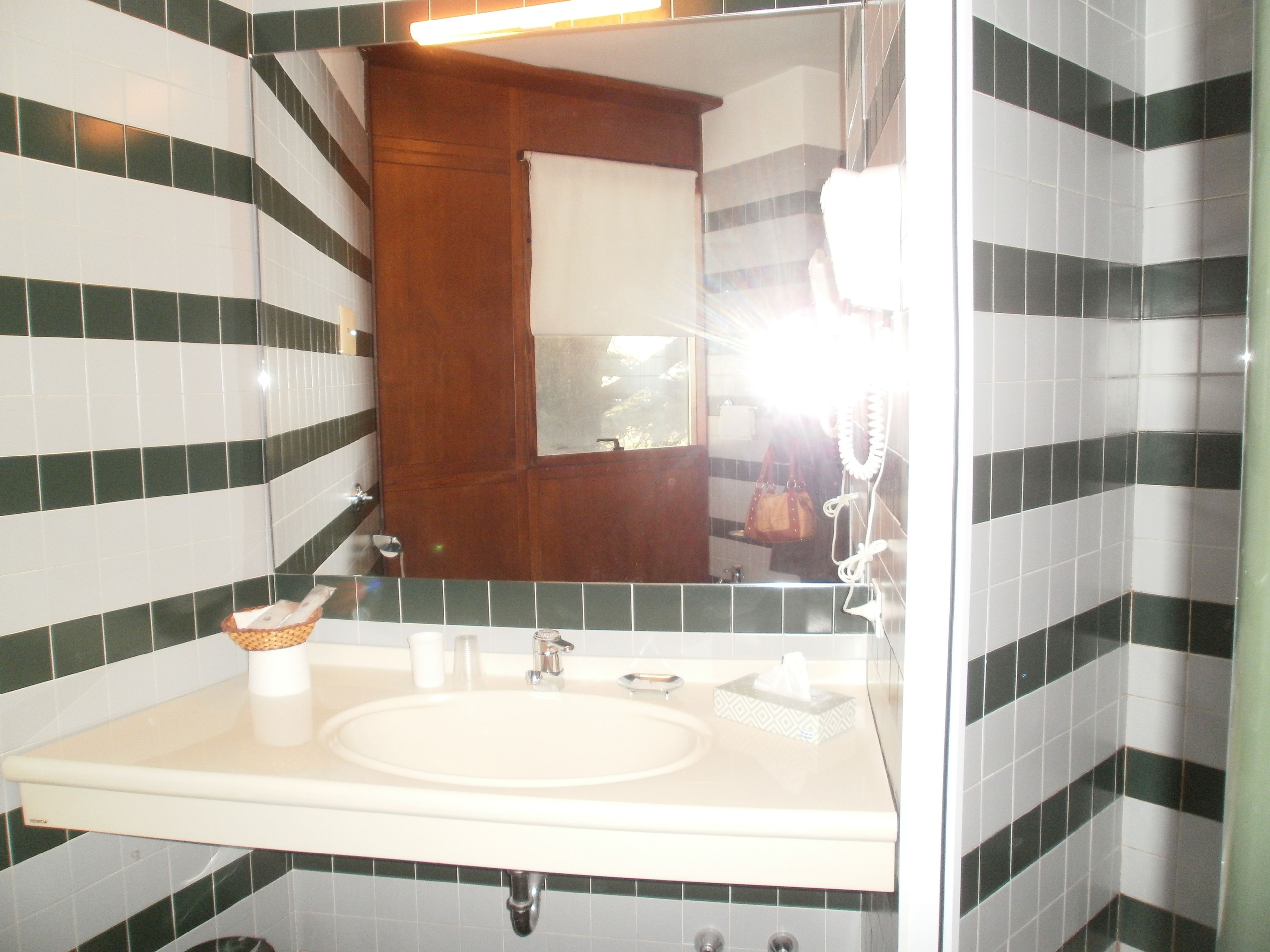 Un bagno con un lavandino bianco, uno specchio e piastrelle a righe verdi e bianche.