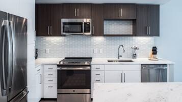 A modern kitchen with stainless steel appliances, white cabinetry, and a tiled backsplash.