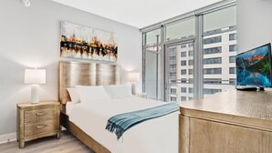 A modern hotel room with a large bed, a desk, a TV, and a cityscape painting on the wall. - Global Luxury Suites Bethesda Chevy Chase (Bethesda)