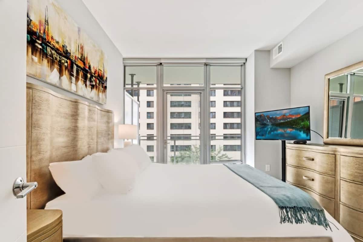 A hotel room with a large bed, a television, a wooden dresser, and a painting on the wall.