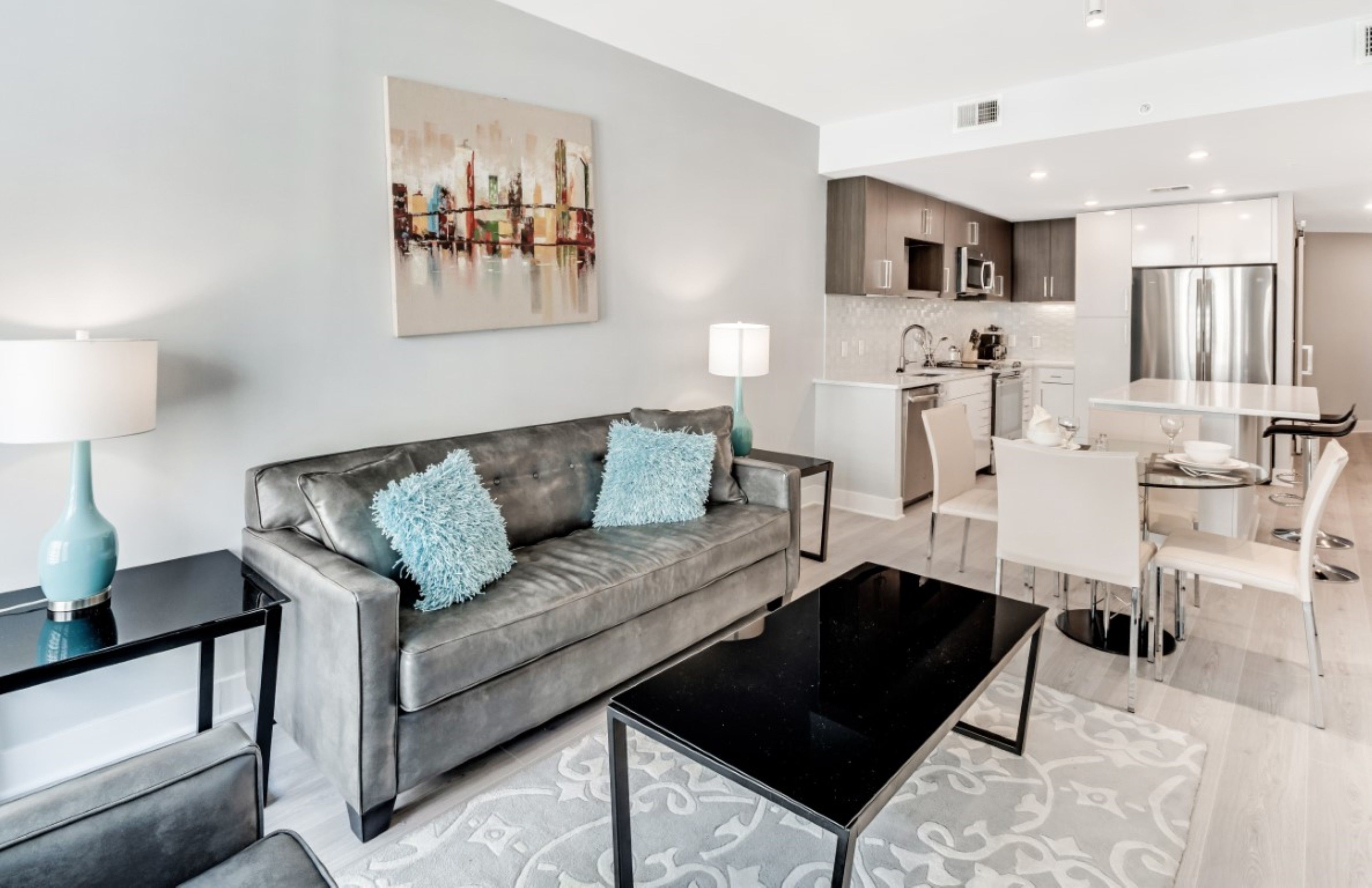 A modern living room with a grey sofa, a black coffee table, and a dining area with a glass table and white chairs.