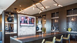 A modern bar area with a marble countertop, bar stools, and a television screen displaying news. - Global Luxury Suites Bethesda Chevy Chase (Bethesda)