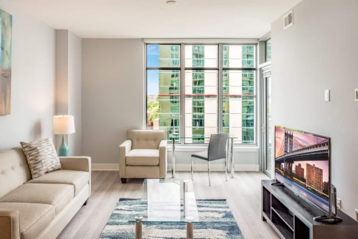 A modern living room with a sofa, a coffee table, a TV, and a large window with a city view.