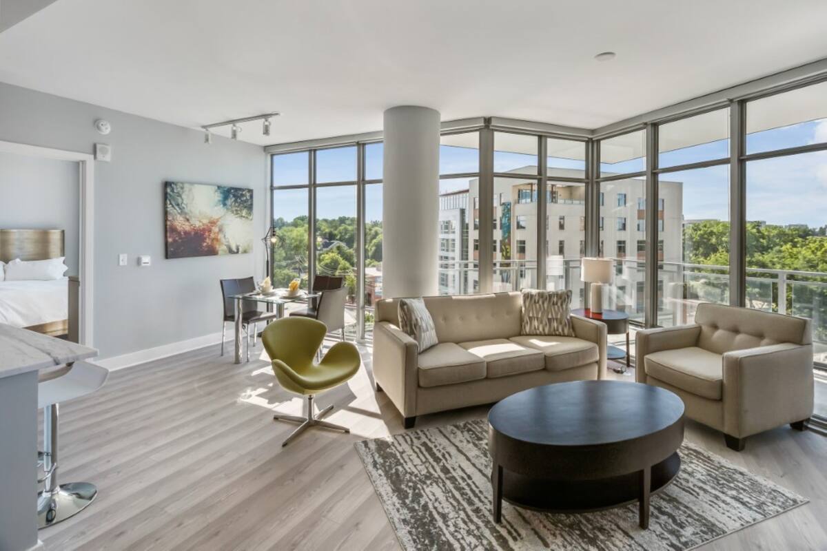 A modern living room with a sofa, armchairs, a coffee table, and a dining area with a table and chairs.