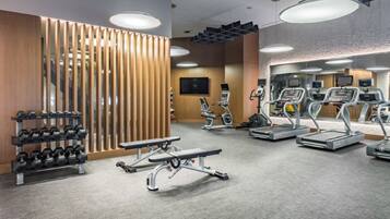 A modern gym with cardio machines, dumbbells, and a bench.
