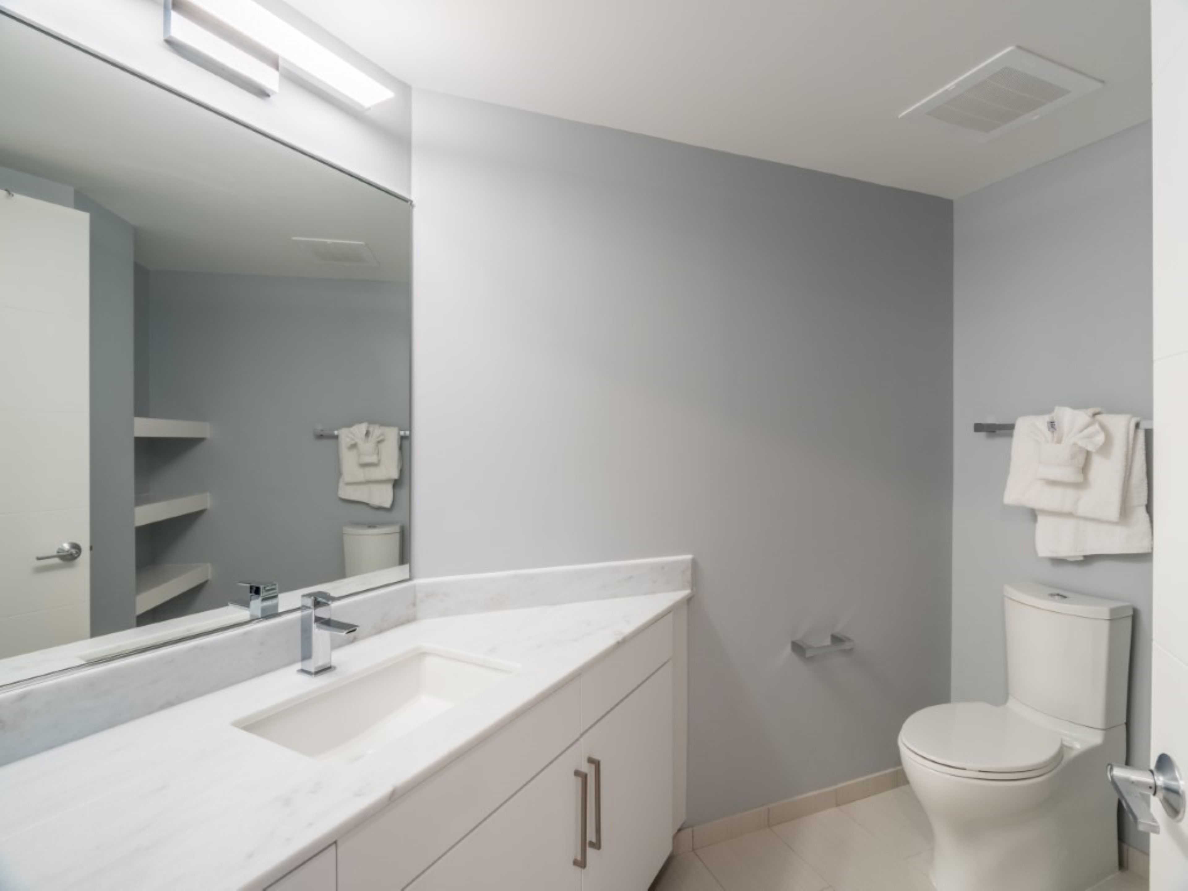Un baño moderno con un tocador blanco, un espejo grande, un inodoro y un perchero para toallas.