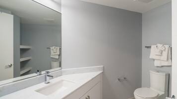 Un baño moderno con un tocador blanco, un espejo grande, un inodoro y un perchero para toallas.
