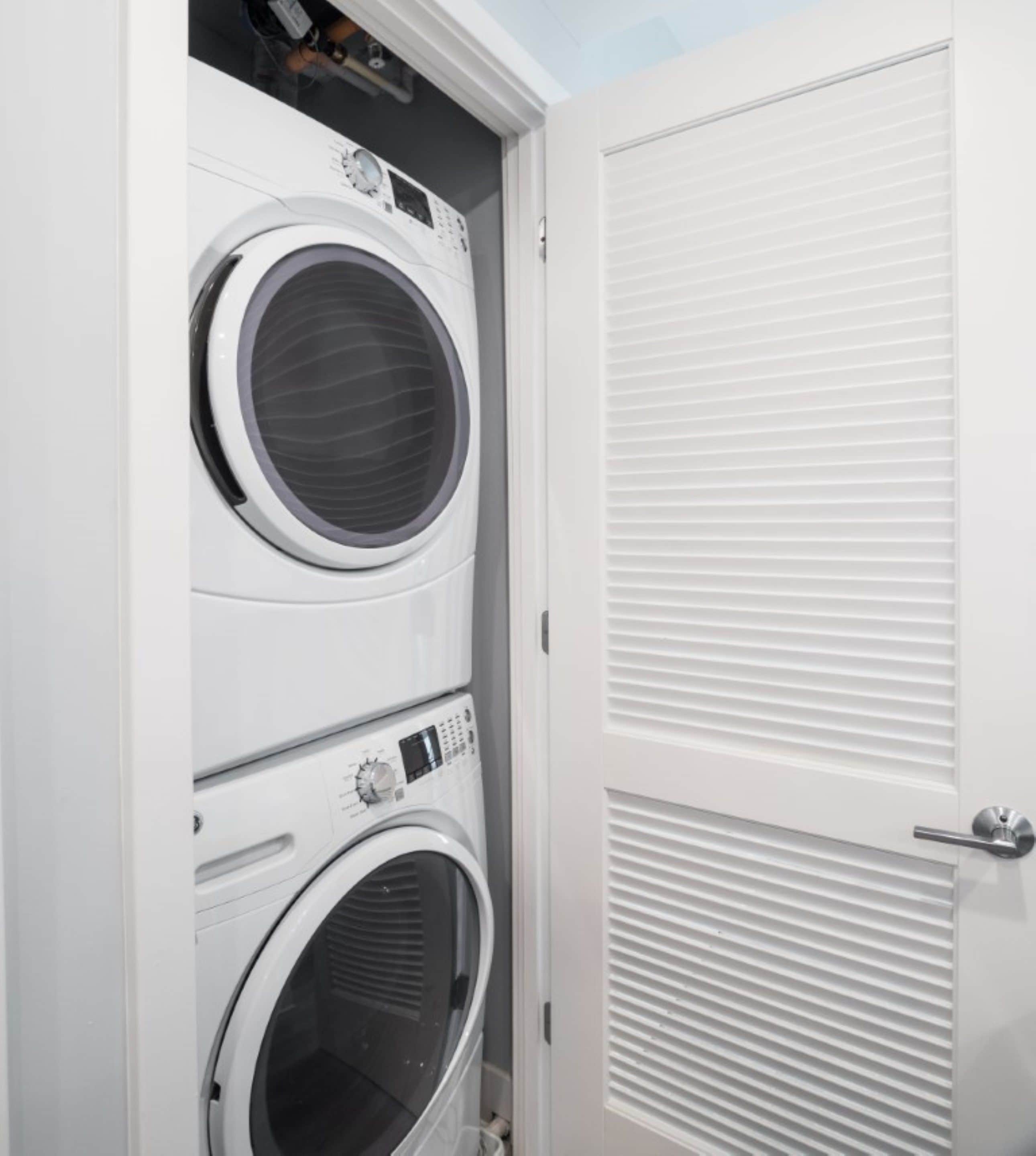 A laundry room with two stacked front-loading washing machines and a white door with horizontal louvered panels.