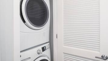 A laundry room with two stacked front-loading washing machines and a white door with horizontal louvered panels.