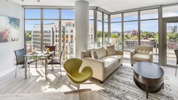 A spacious living room with large windows, a modern sofa, a round coffee table, and a dining area with a glass table and chairs. - Global Luxury Suites Bethesda Chevy Chase (Bethesda)