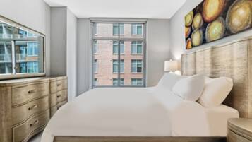 A modern hotel room with a large bed, a wooden dresser, a window with a city view, and a painting on the wall.