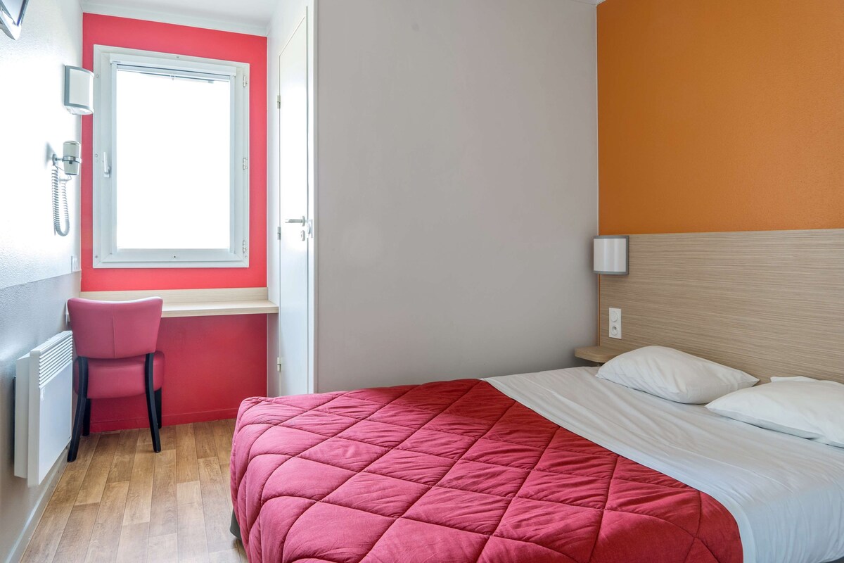 A bedroom with a bed, a desk, a chair, and a window.