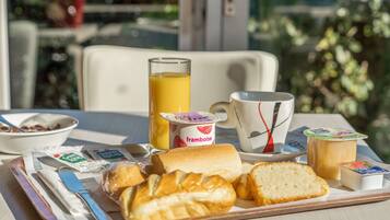 Bandeja de desayuno con pan, mantequilla, mermelada, un vaso de jugo de naranja, una taza y un tazón de cereal.
