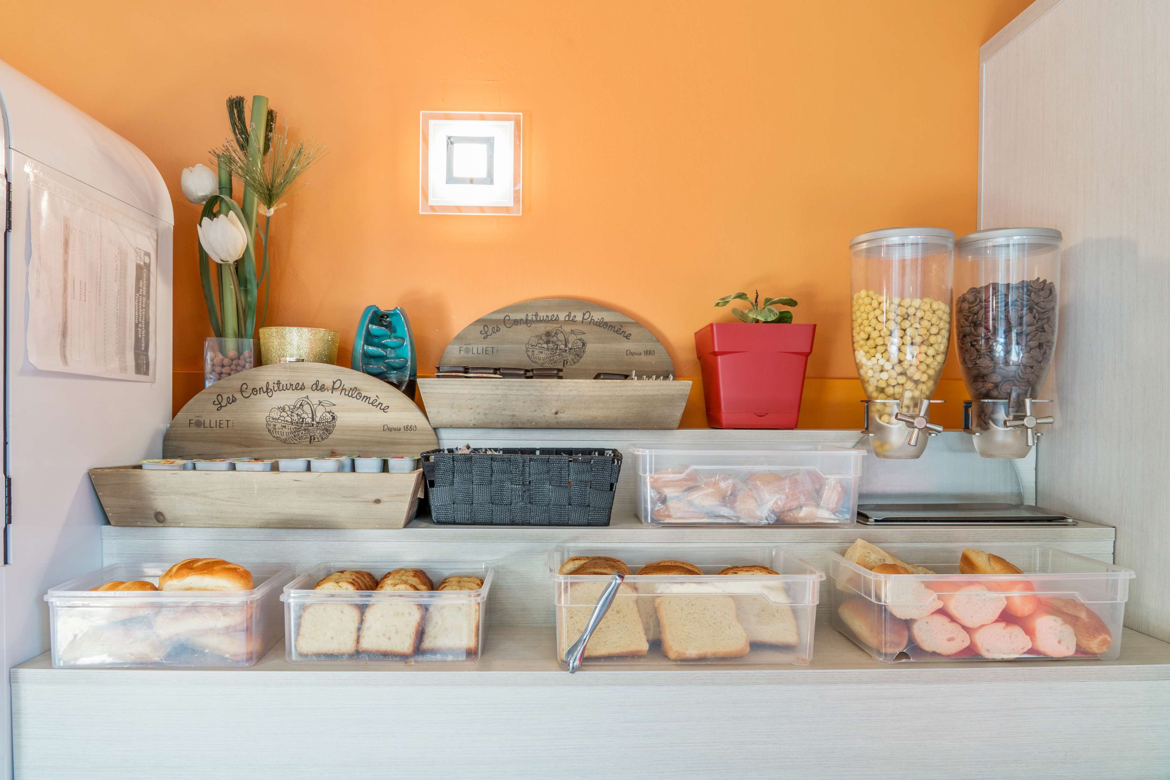 Una cuina amb taulell, diversos aliments i recipients, incloent pa, una màquina de cafè i un rètol decoratiu.