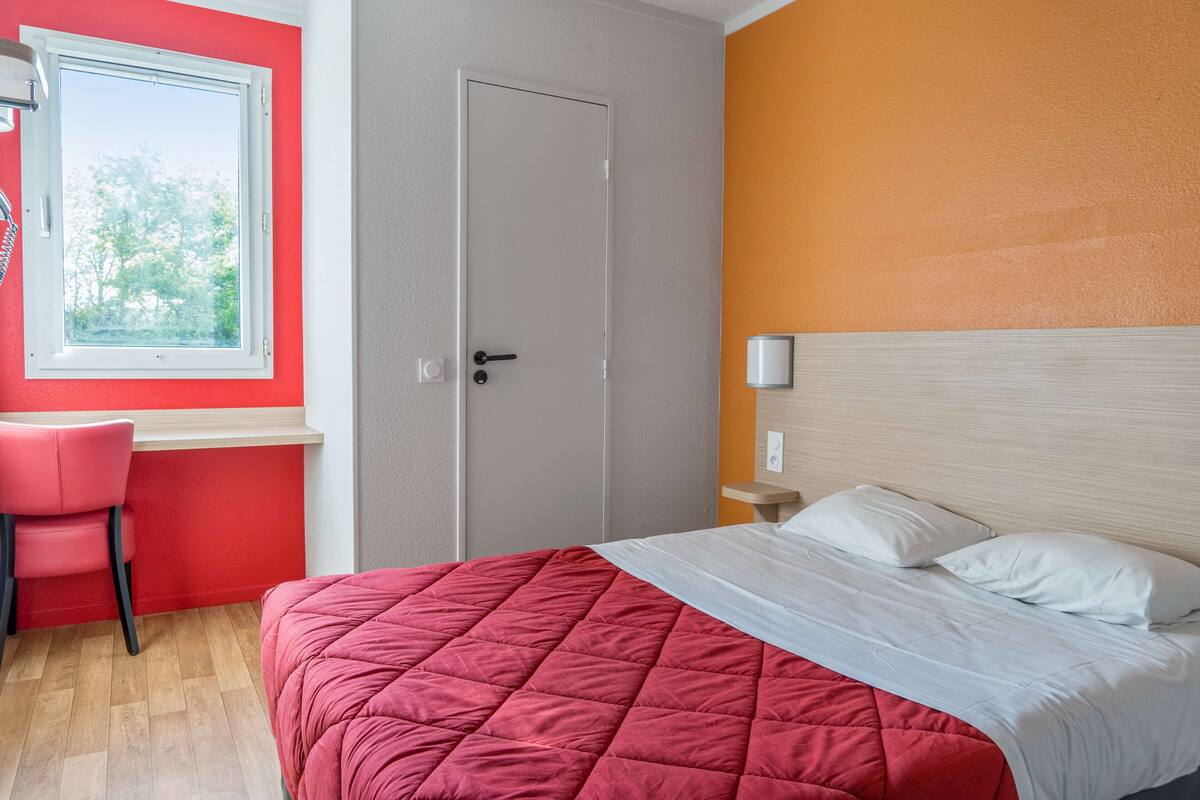 Una habitación de hotel con cama, escritorio y ventana.