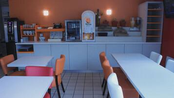 A restaurant with white tables and orange chairs, a coffee machine, and a refrigerator.