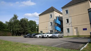 A parking lot with several cars and a building with a blue facade and a sign that reads "ACQUA". - PREMIERE CLASSE ROUEN NORD - Barentin (Barentin)