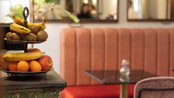 Un comedor con una mesa de vidrio, un banco acolchado rojo y una pila de frutas sobre la mesa.