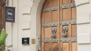 Un'ampia porta in legno con rinforzi metallici, una pianta in vaso e un cartello con la scritta 'We'.