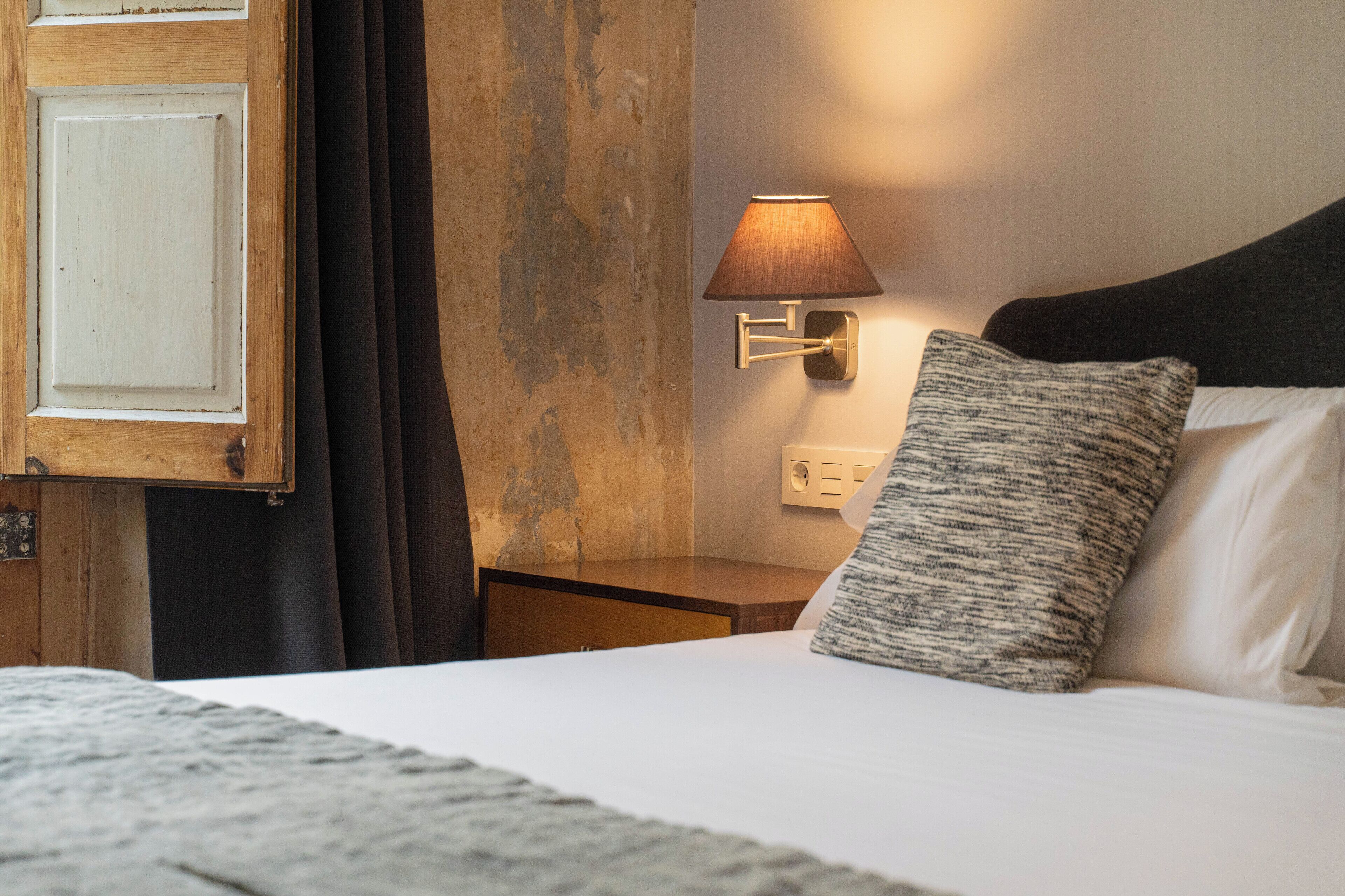 Een hotelkamer met een bed, een wandlamp, een houten deur en een gestructureerd kussen.